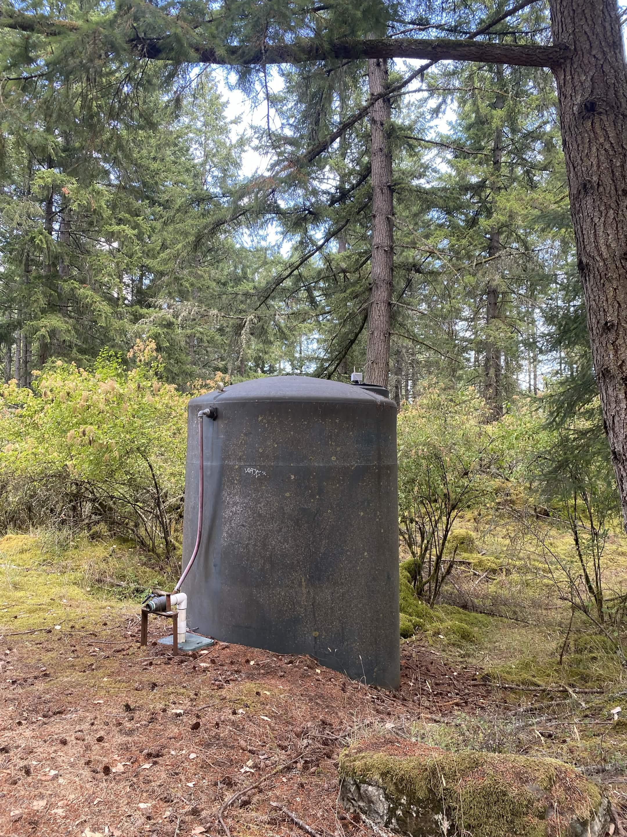 A water cistern installed at a wooded rural site, with outlet piping at its base